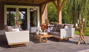 Two woman sit on their patio furniture on a sunny day while one of them plays the guitar.